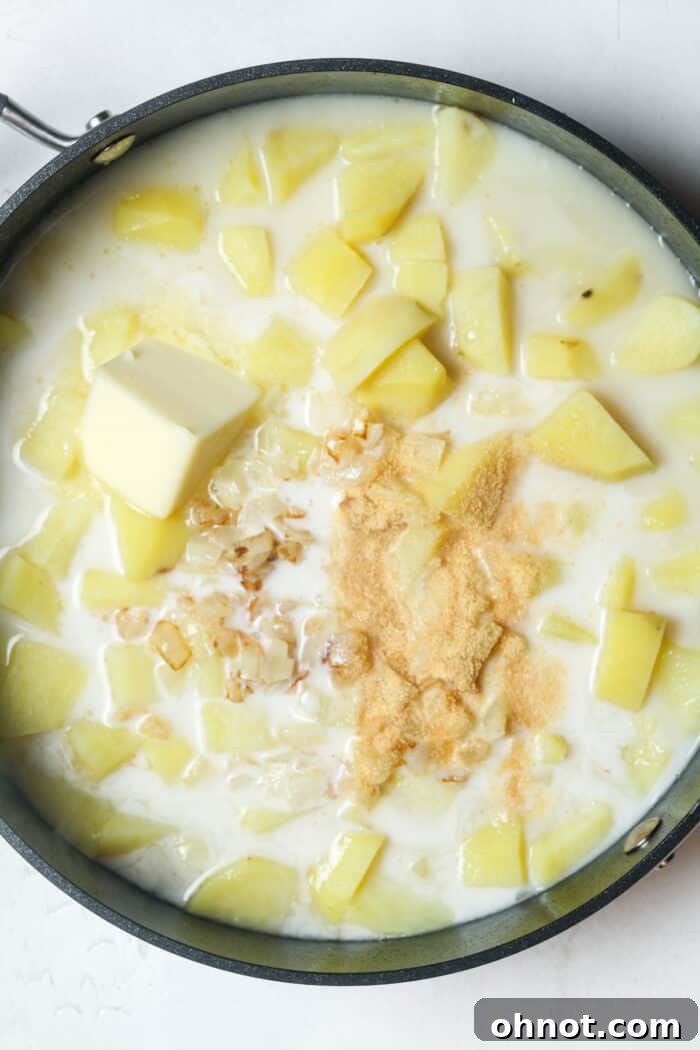 Cooked potatoes, melted butter, milk, and garlic powder stirred together in a skillet.