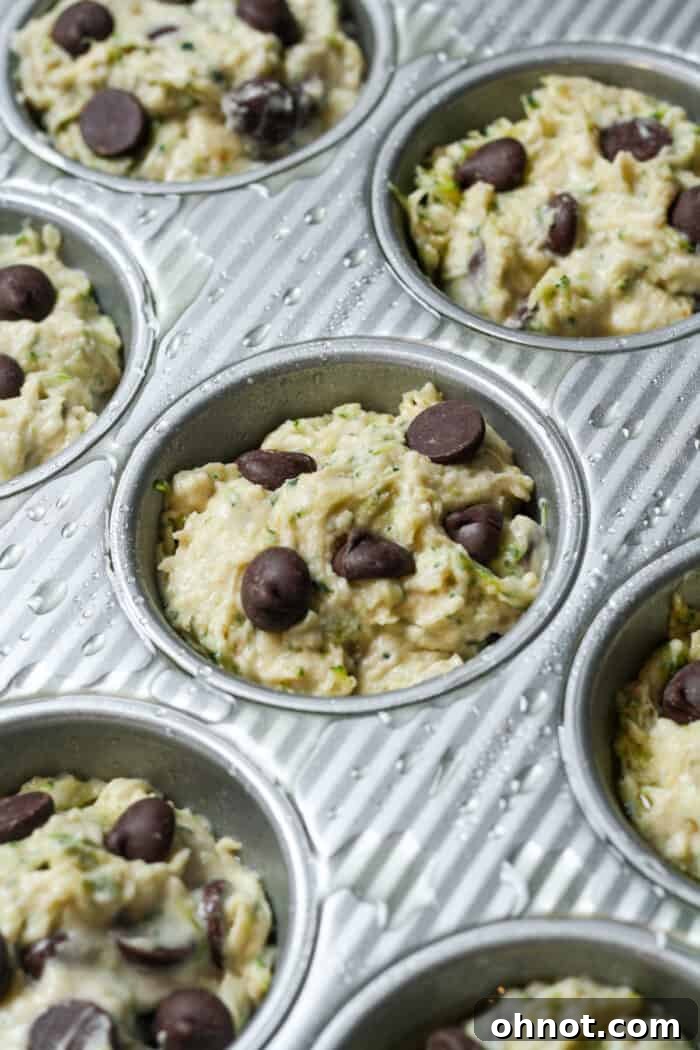 Zucchini muffin batter neatly portioned into a muffin pan, ready for the oven.