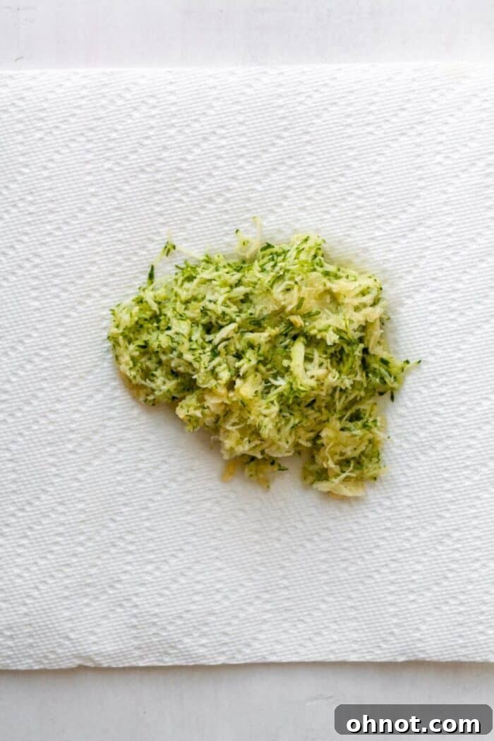 Finely grated zucchini spread on a paper towel, illustrating the first step of moisture removal.