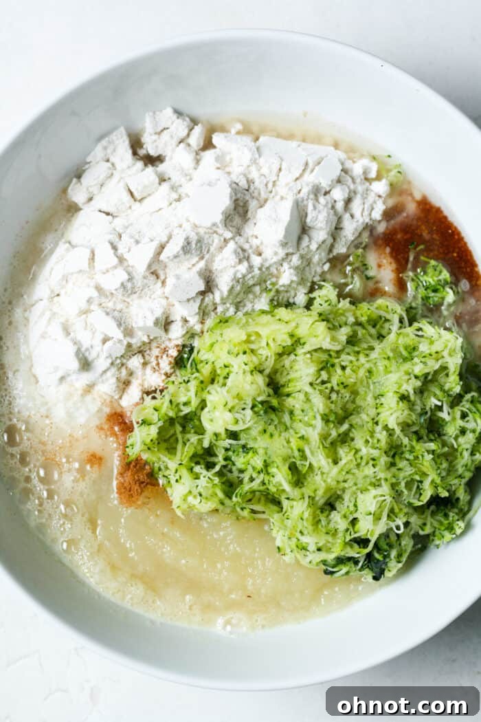 A mixing bowl with grated zucchini and flour, among other ingredients, before mixing into batter.