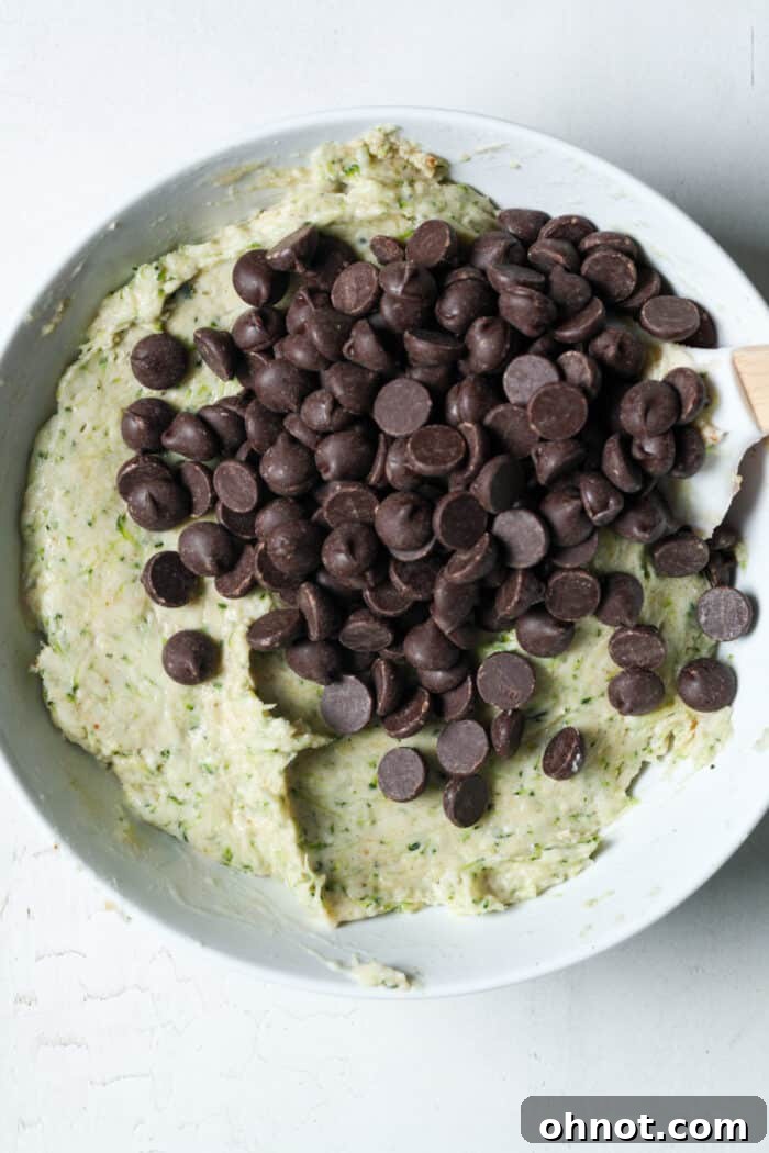 Zucchini muffin batter with dark chocolate chips folded in, showing even distribution.