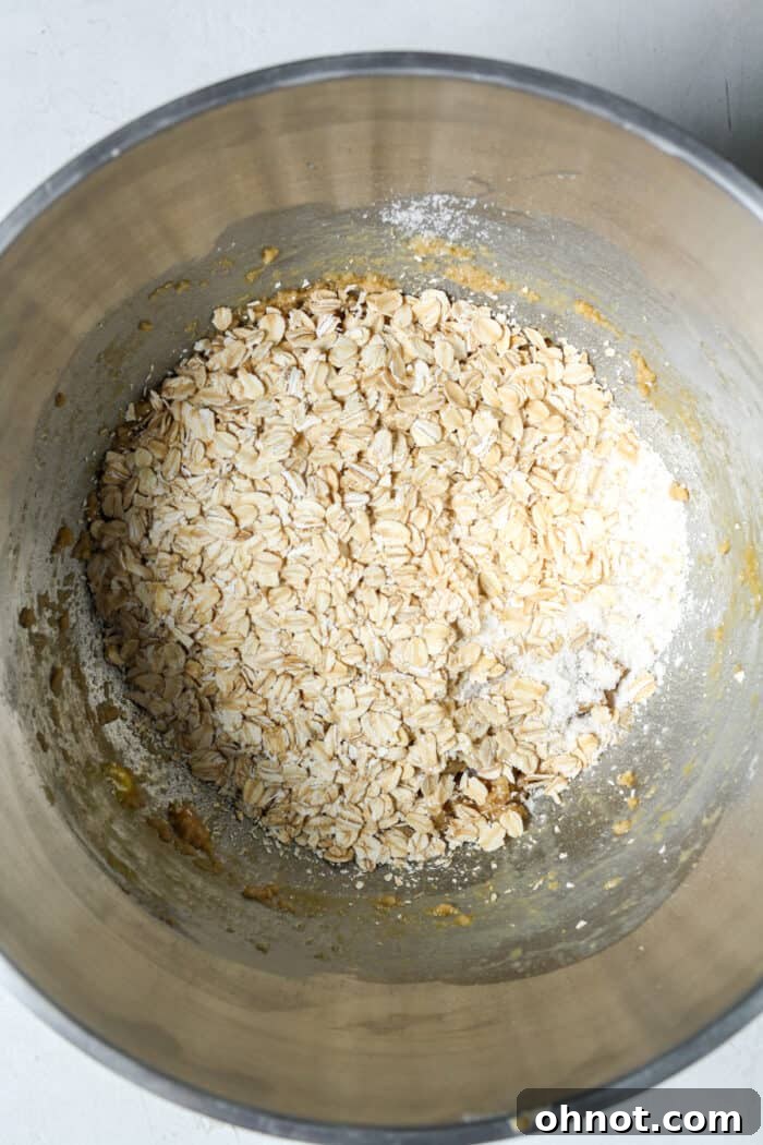 Rolled oats and other dry ingredients added to the dough in a mixing bowl.