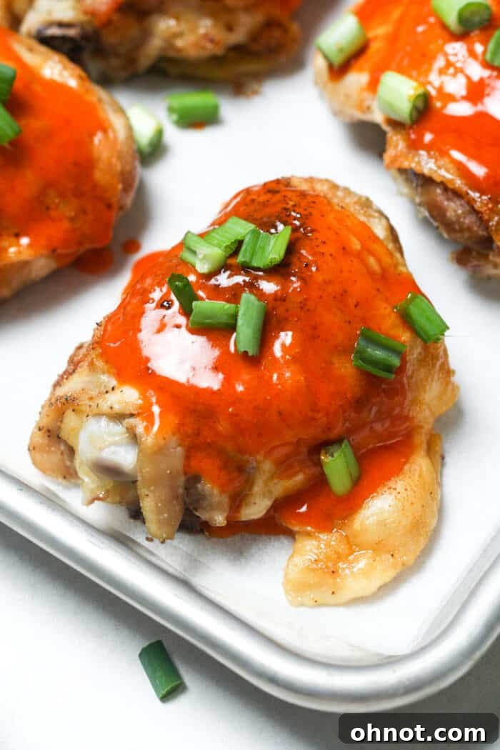 Oven-baked buffalo chicken thighs, served on a white platter, garnished with fresh herbs.