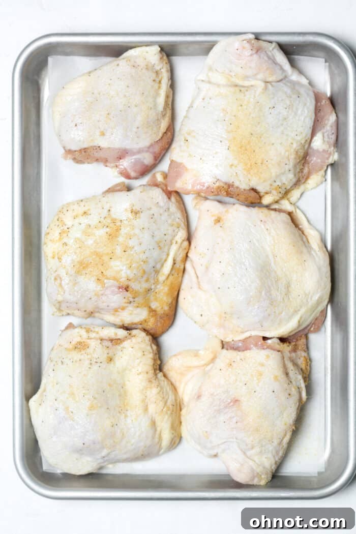 Seasoned chicken thighs laid out on a baking pan, ready to go into the oven.