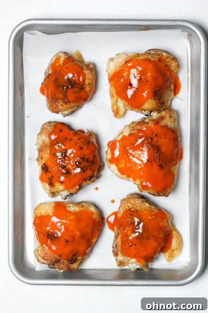 Spicy buffalo chicken thighs brushed with sauce on a pan, garnished with green onions.
