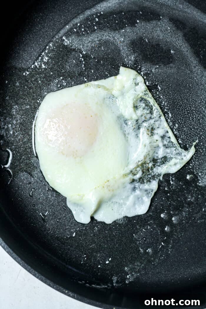 Fried egg in skillet after being flipped, cooking on the second side