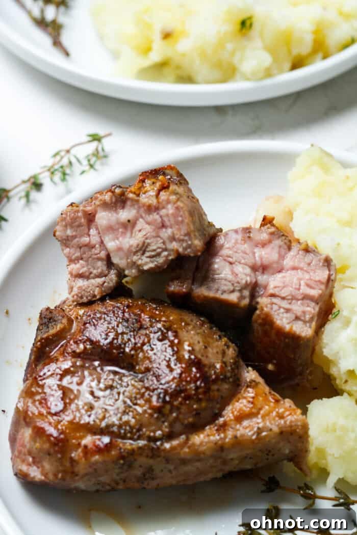 Two medium-rare lamb chops, perfectly seared and rested, served on a white plate with a side of green vegetables and a sprig of fresh rosemary.