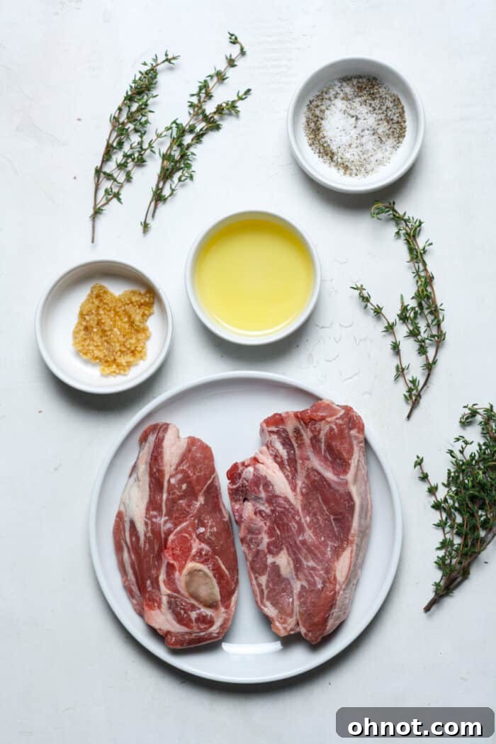 Raw lamb chops, fresh rosemary sprigs, and minced garlic laid out on white plates, with a small bowl of olive oil, ready for seasoning and sous vide preparation.