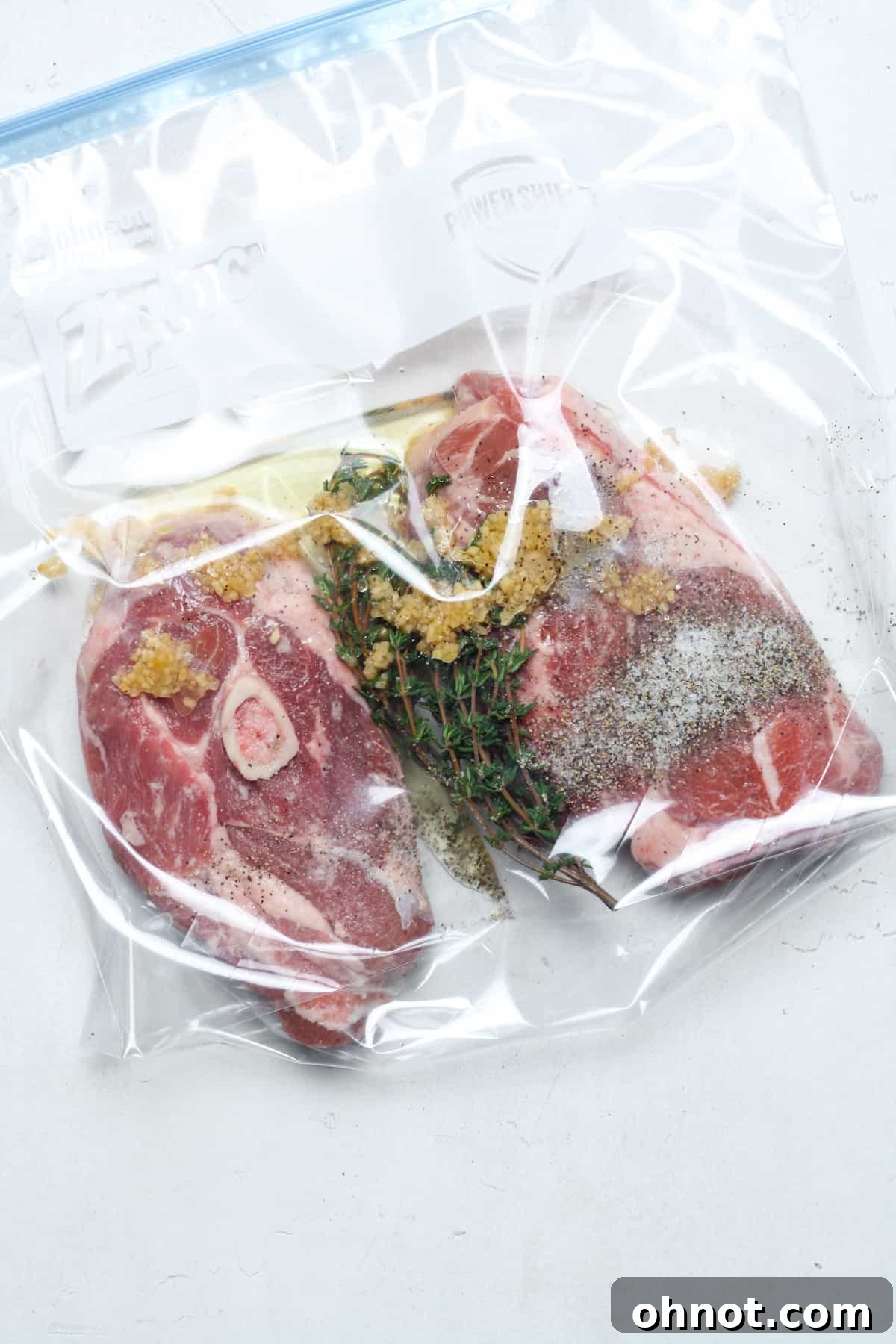 Raw lamb chops seasoned with oil, salt, pepper, garlic, and rosemary, placed inside a zippered bag, ready for sealing and immersion in a sous vide water bath.