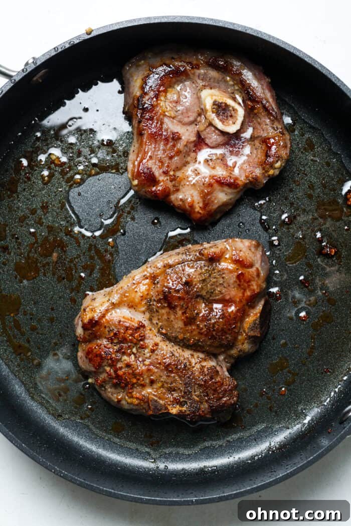 Golden-brown seared lamb chops sizzling in a hot cast iron skillet, developing a crispy crust after their sous vide bath.
