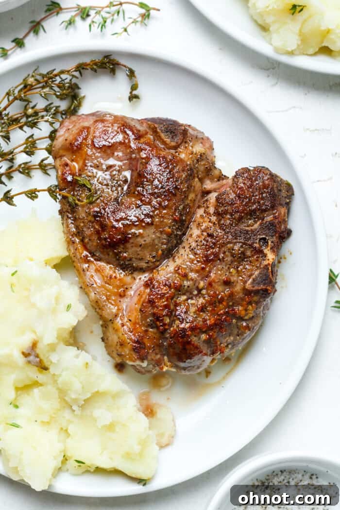 A perfectly seared medium-rare lamb chop served on a plate with creamy mashed potatoes and green vegetables, garnished with rosemary.
