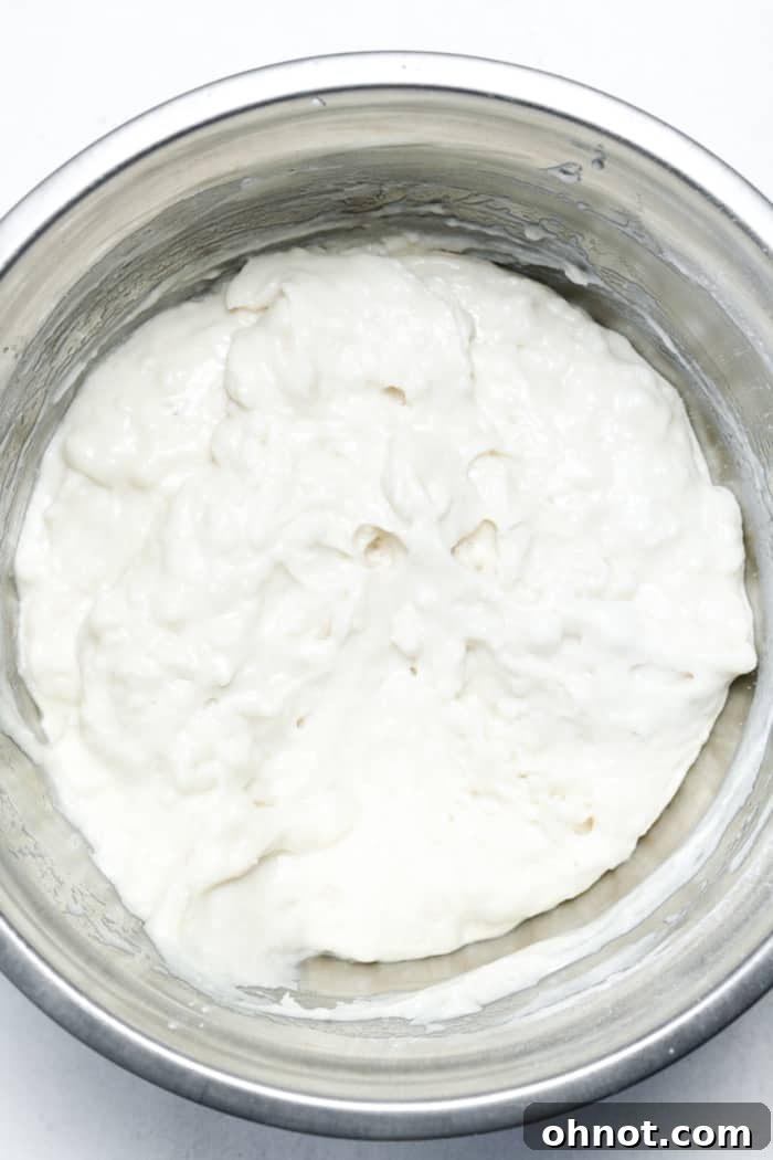 A thick cake batter, perfectly mixed and ready for layering, sits in a large mixing bowl, highlighting its rich consistency.