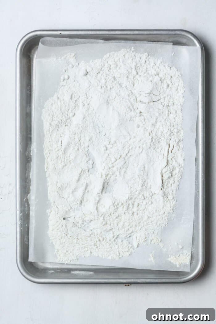 Raw flour evenly spread on a parchment-lined baking pan, prepared for heat treating to ensure food safety