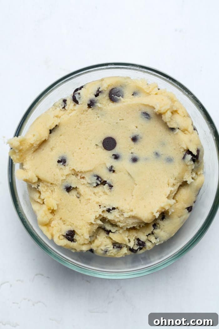 A bowl of freshly mixed edible cookie dough, rich with mini chocolate chips, ready to be rolled into individual bites