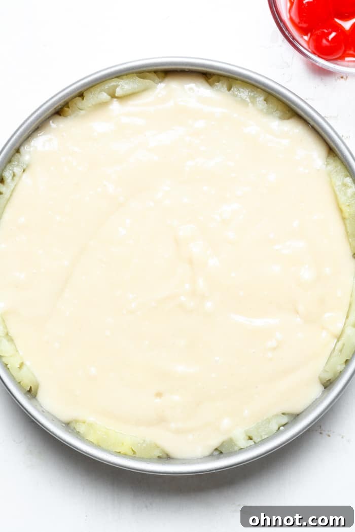 Cake batter poured over the pineapple and cherries in the cake pan.