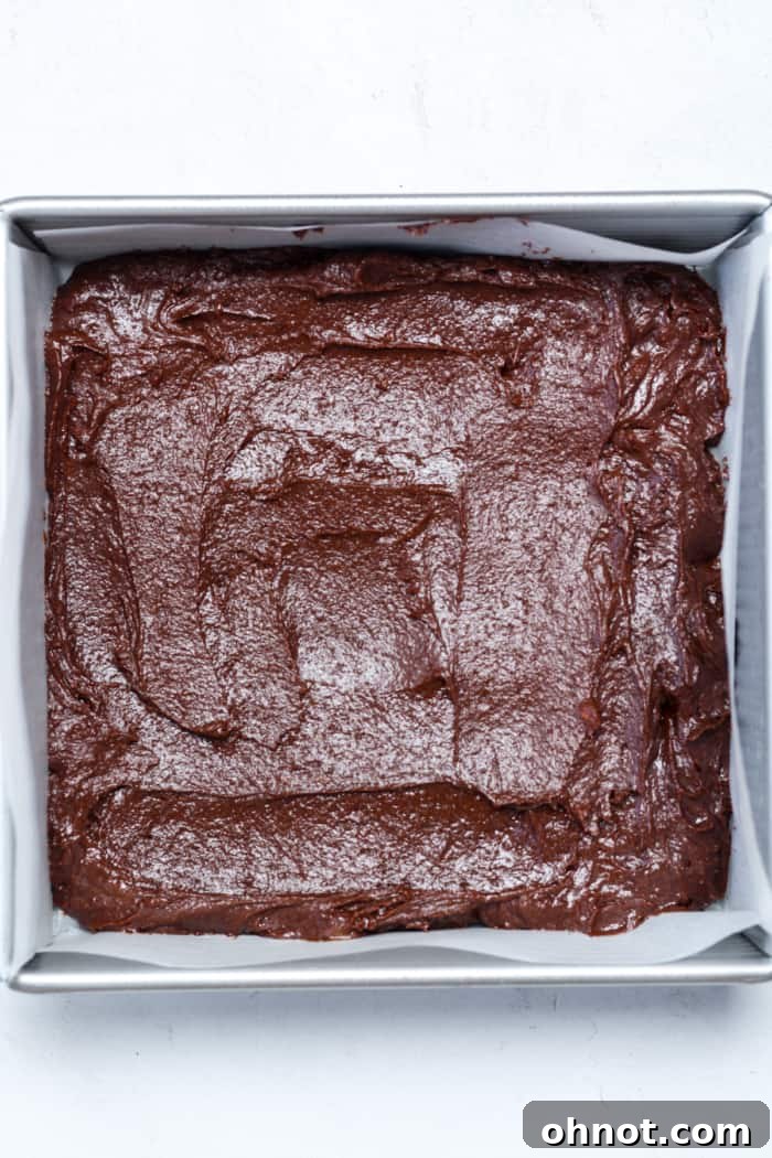 Raw gluten-free brownie batter evenly spread in a parchment-lined baking pan