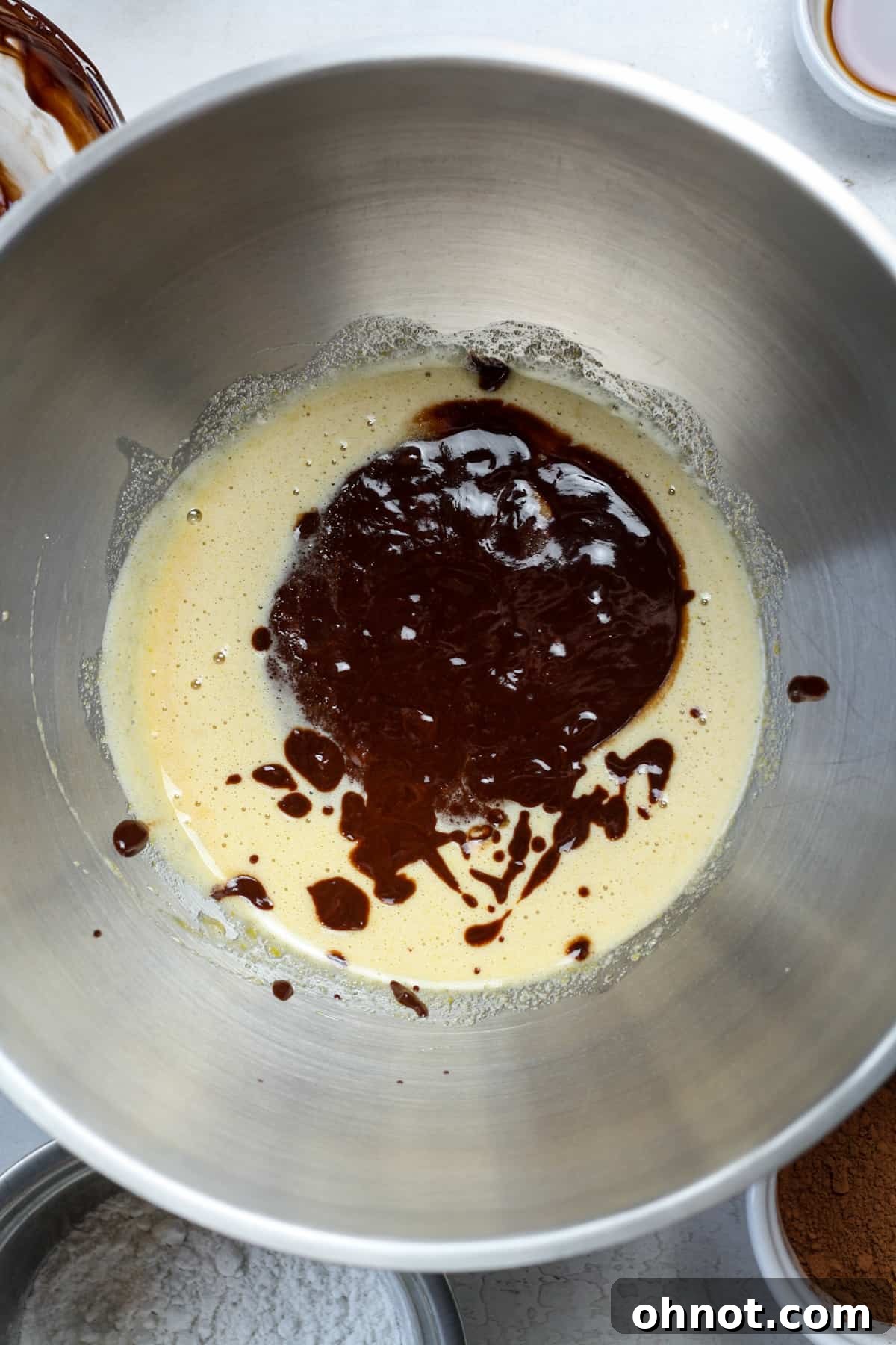 Melted chocolate mixture being poured into the beaten eggs and sugars