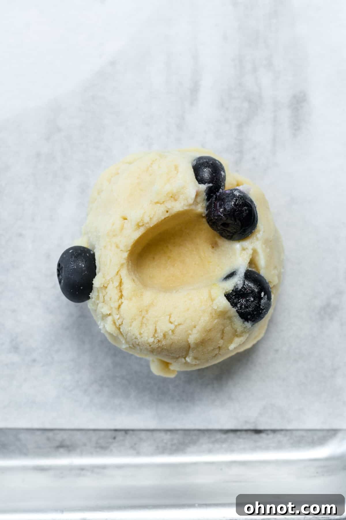 Several balls of blueberry cookie dough on a baking sheet, each with a thumb indent in the center.