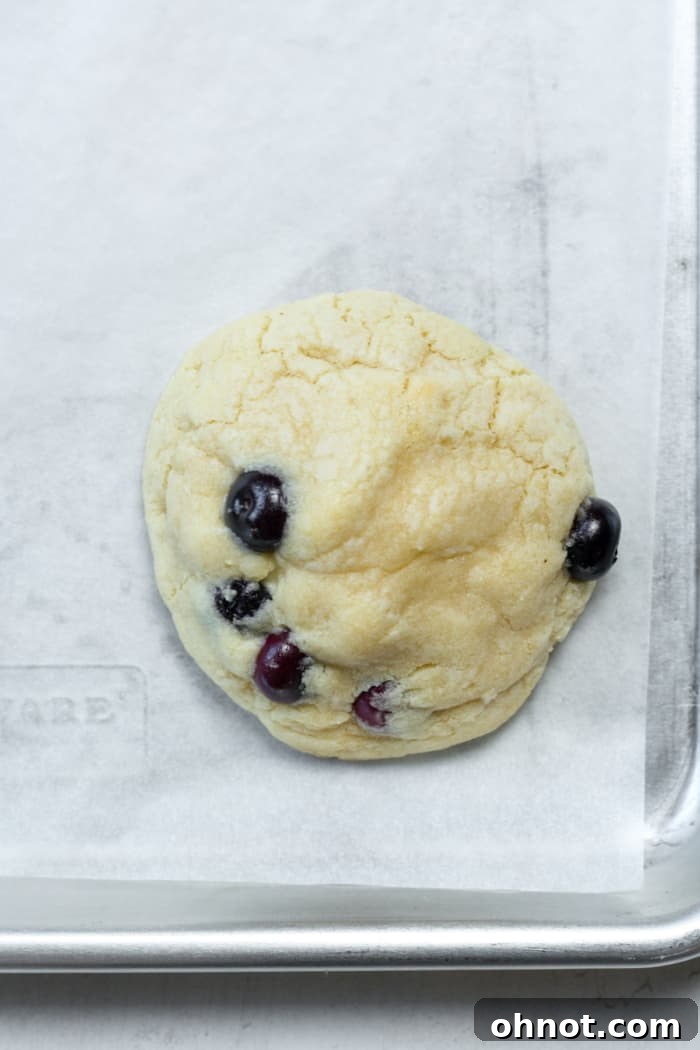 Freshly baked blueberry cheesecake cookies on a baking sheet, with a golden edge and gooey centers.