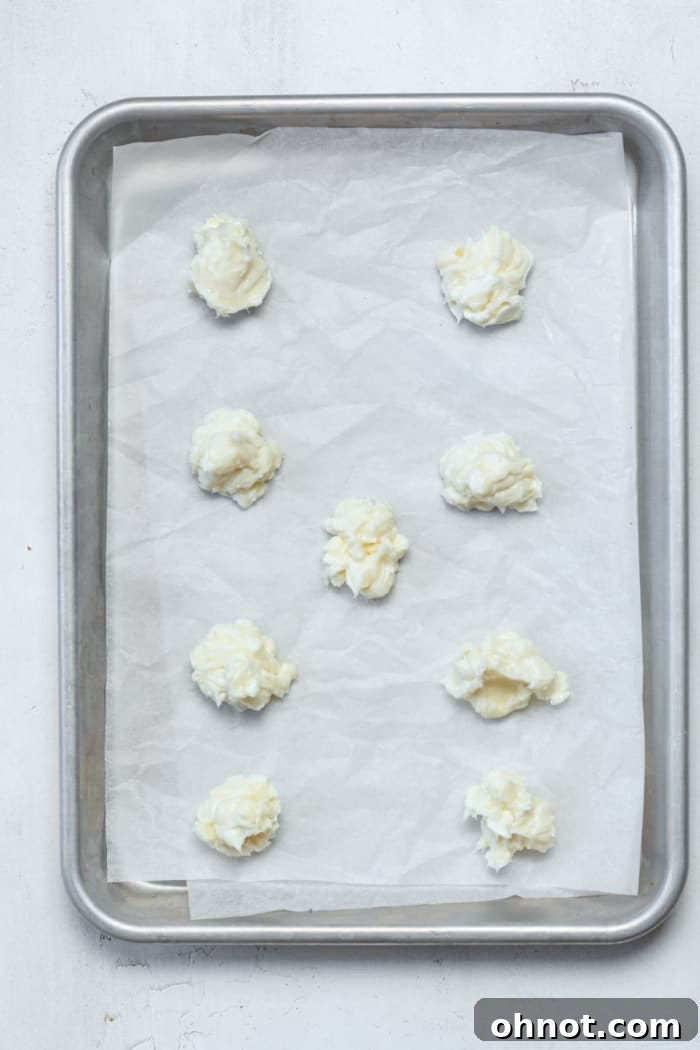 Small, uniformly sized balls of cream cheese filling placed on a parchment-lined pan, ready for freezing.