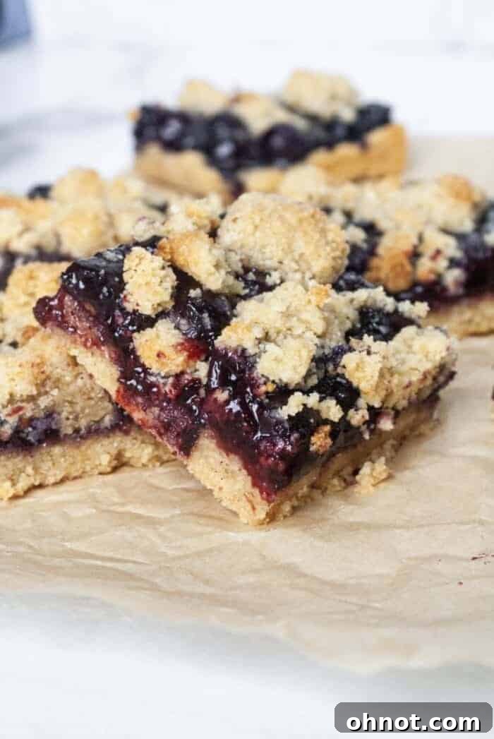 A single Paleo Blueberry Crumb Bar artfully placed on a sheet of beige parchment paper, showcasing its golden crust, vibrant blueberry filling, and delicate crumb topping.