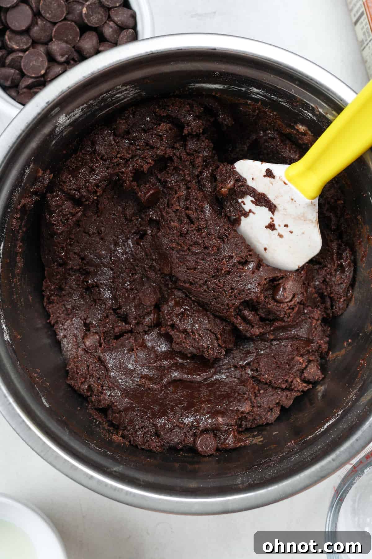 A perfectly thick and glossy chocolate cookie dough formed in a bowl, showcasing its rich brown color.