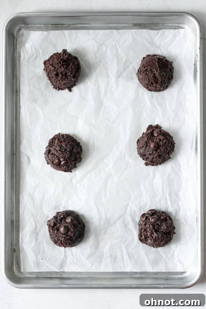 Unbaked chocolate cookie dough scooped onto a parchment-lined baking pan, ready for the oven.