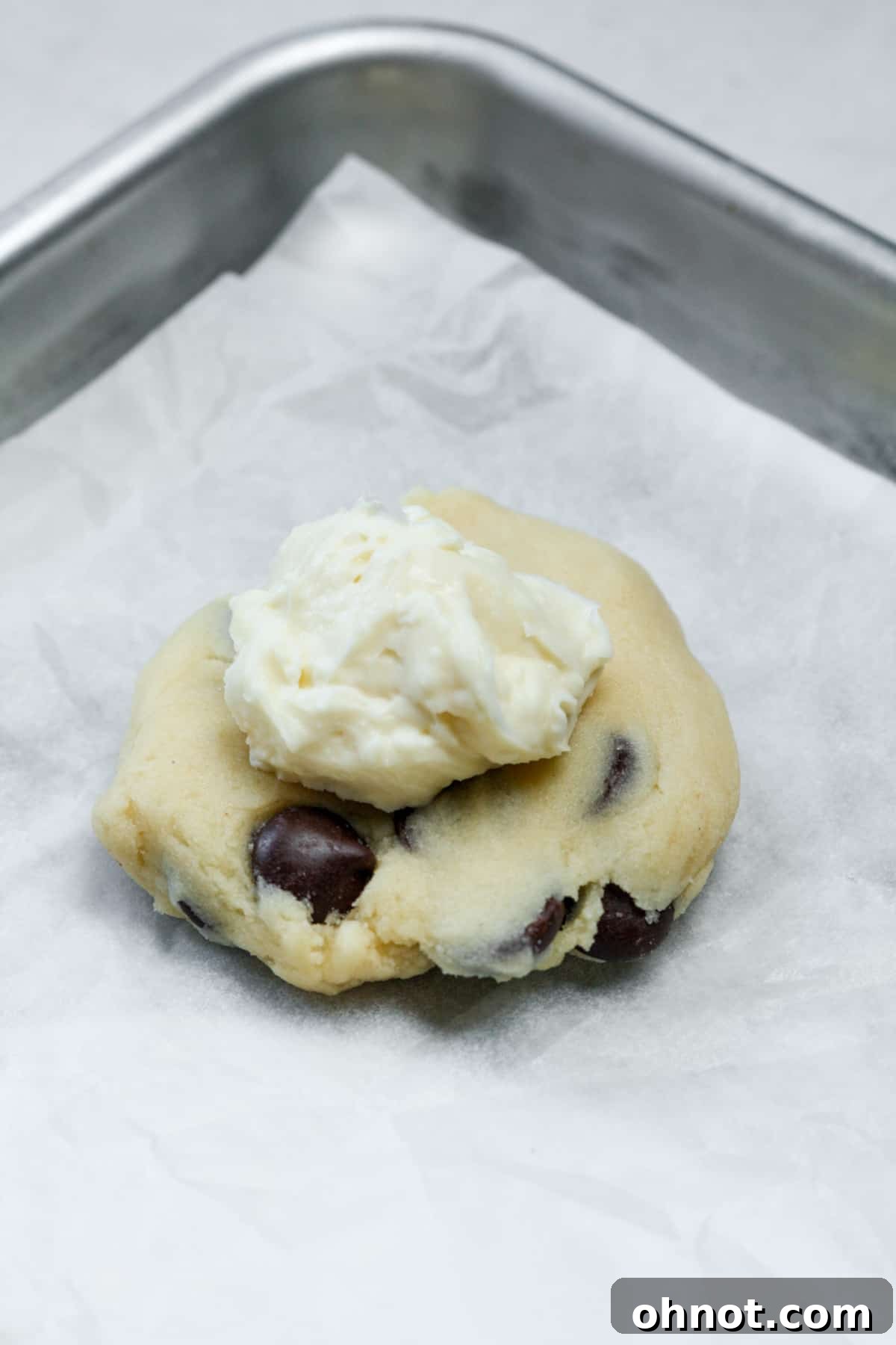 A frozen cheesecake ball placed precisely onto the center of a flattened cookie dough disc.