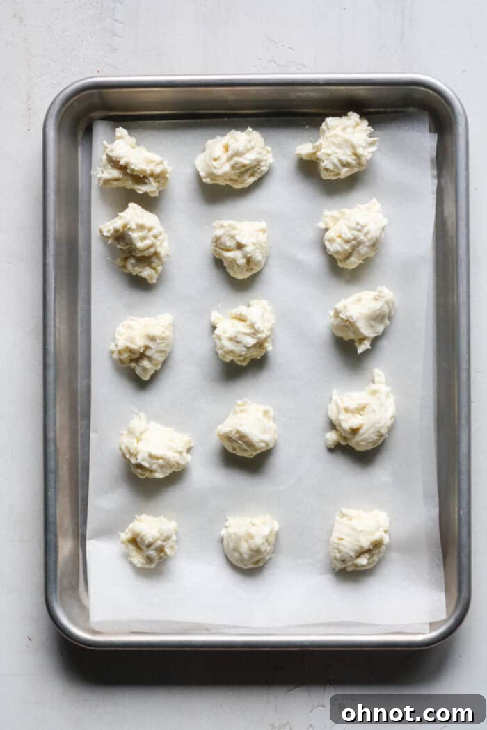 Small, perfectly rounded balls of cheesecake filling arranged on a parchment-lined pan, ready for freezing.