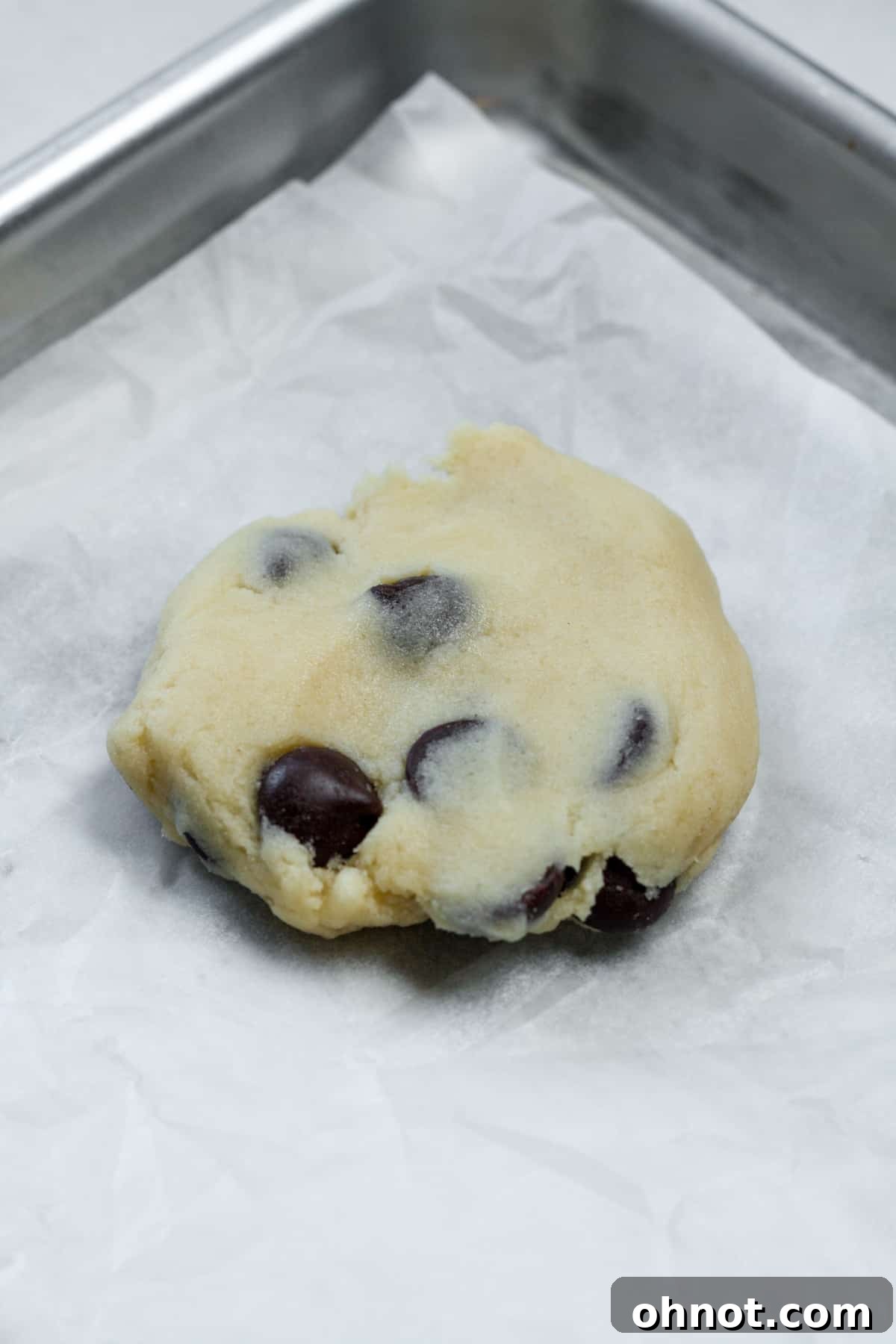 A flattened piece of chocolate chip cookie dough, forming the base for the cheesecake filling.