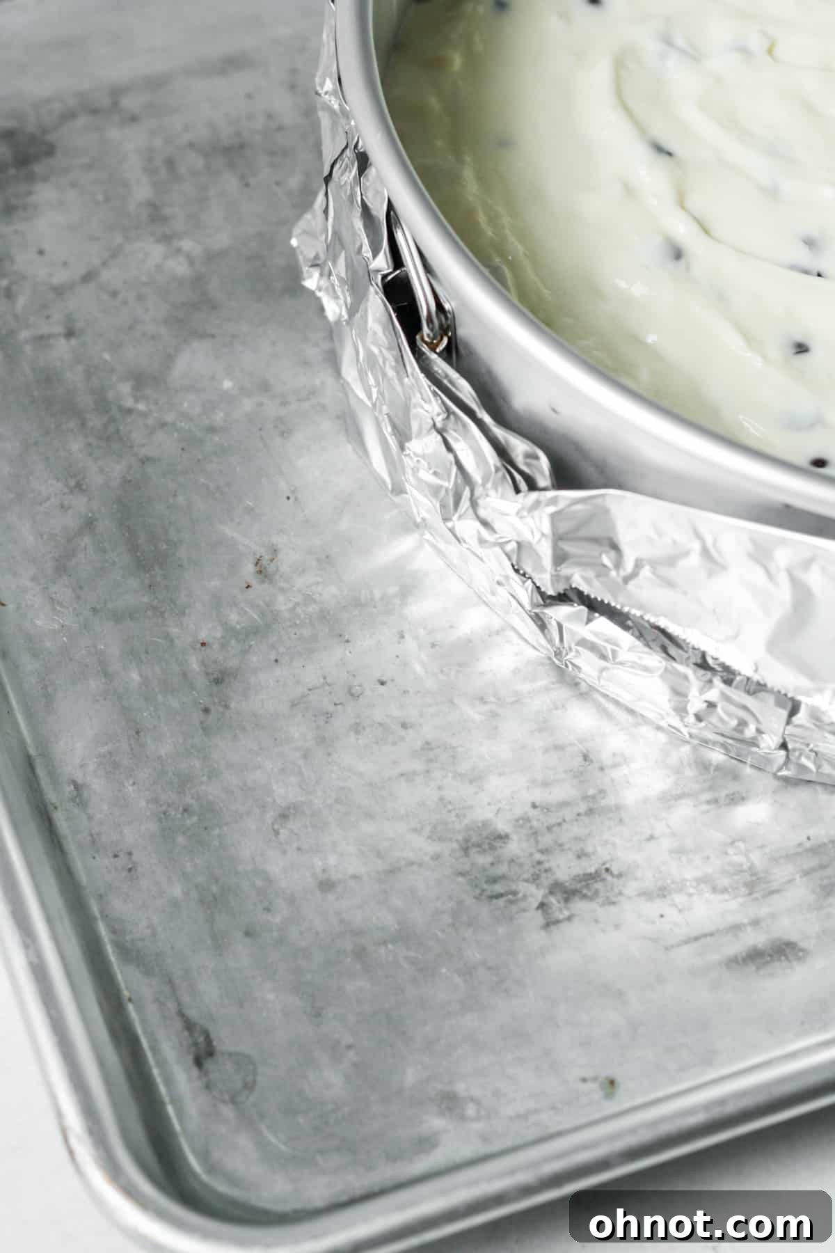 Boiling water being carefully poured into a roasting pan around the springform pan for the cheesecake water bath.