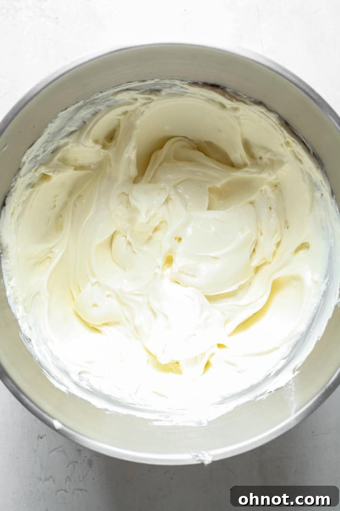 A creamy, white cheesecake batter in a mixing bowl after combining all ingredients except eggs and chocolate chips.
