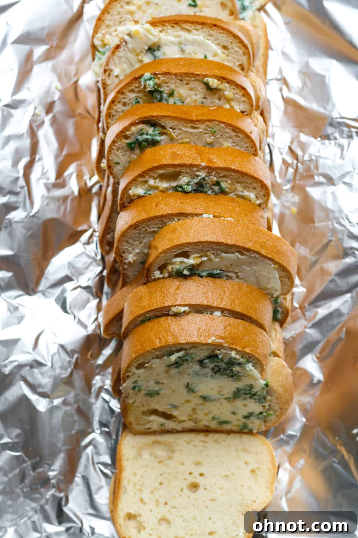 A whole loaf of gluten-free bread, sliced and spread with garlic butter, ready for baking.