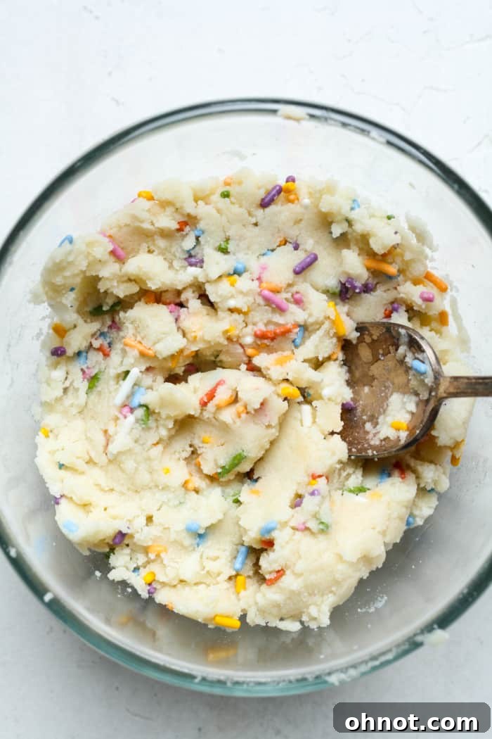 Colorful sprinkles being folded into the smooth sugar cookie dough.