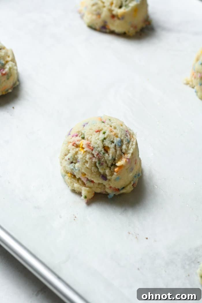 Evenly scooped balls of sprinkle cookie dough placed on a parchment-lined baking sheet.