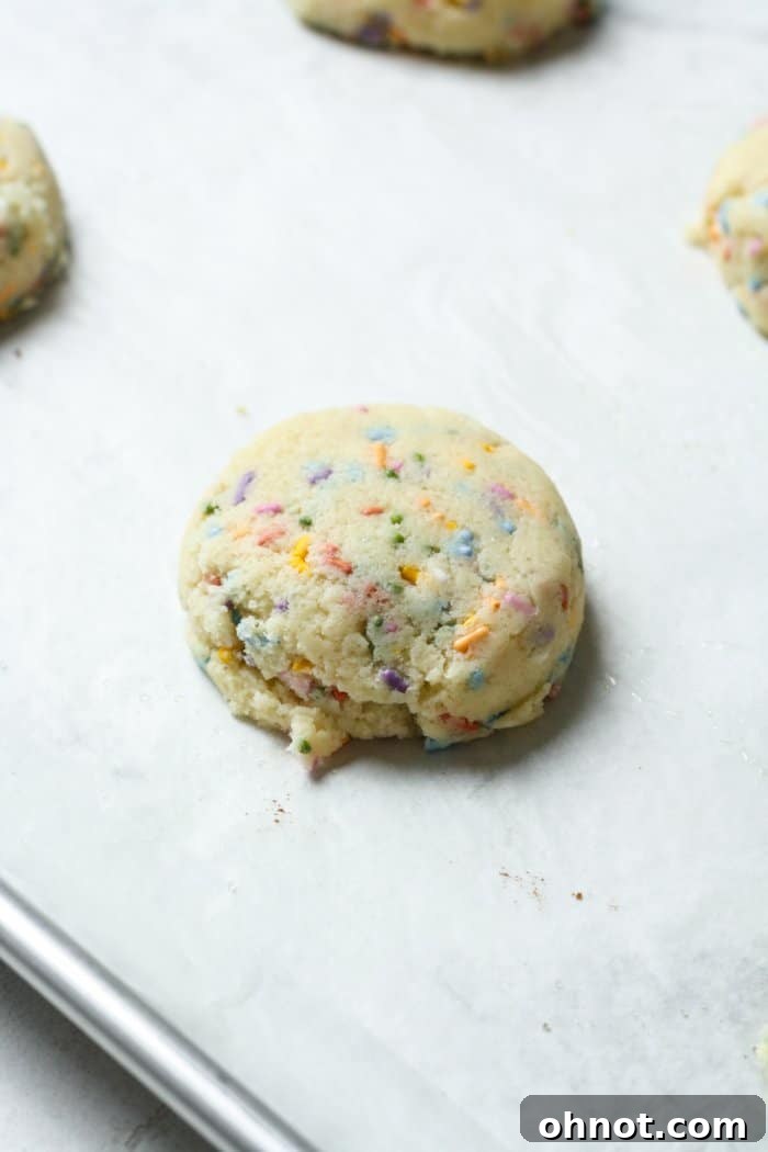 Flattened balls of cookie dough with sprinkles arranged on a baking pan, ready for the oven.