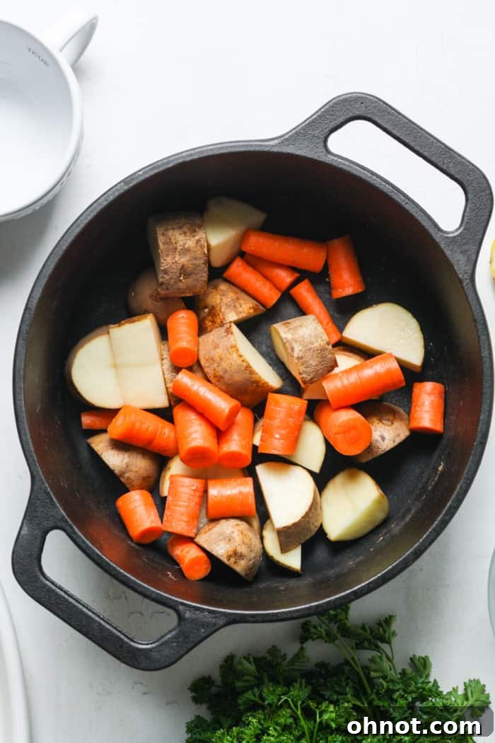Cubed potatoes and chopped carrots seasoned and placed in a Dutch oven
