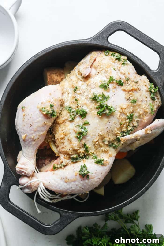 Whole raw chicken placed breast-side up over vegetables in a Dutch oven