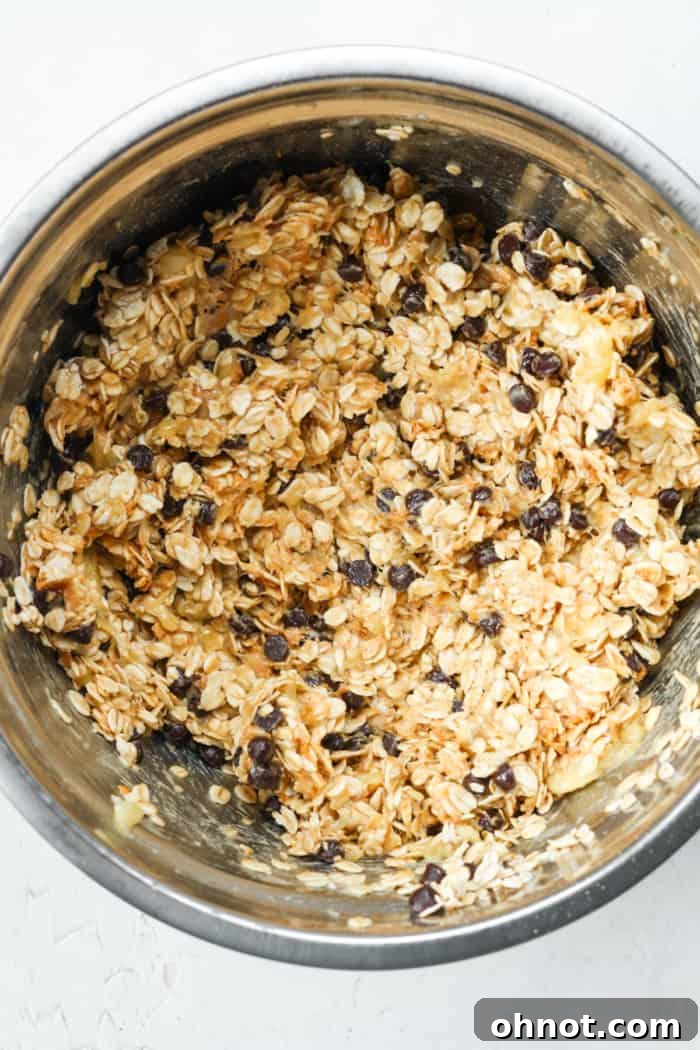 Thick cookie batter made from bananas, oats, peanut butter, and chocolate chips in a mixing bowl.