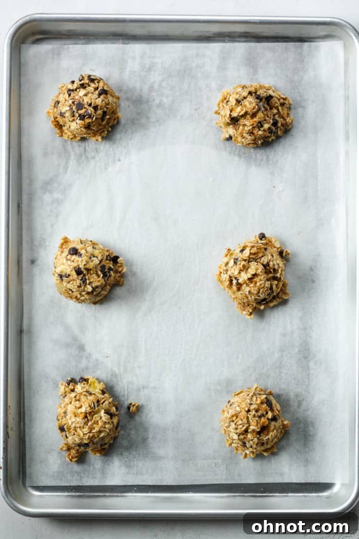 Scooped balls of oatmeal cookie dough ready on a parchment-lined baking pan.