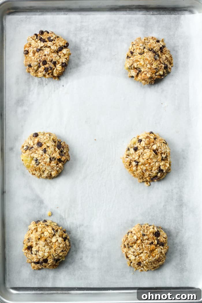 Flattened 4 ingredient banana oatmeal cookies placed on a baking sheet before baking.