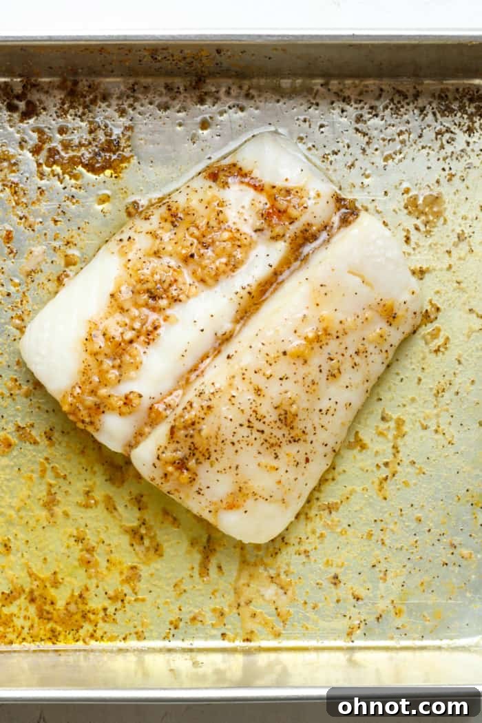A golden-brown baked halibut fillet resting in a pan, glistening with melted garlic butter after cooking.
