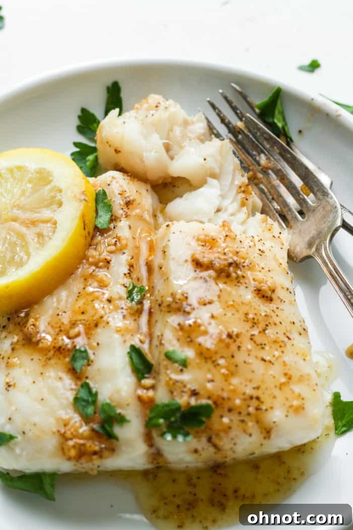 Close-up of flaky baked halibut on a white plate, showing its perfectly cooked, tender texture and moist interior.