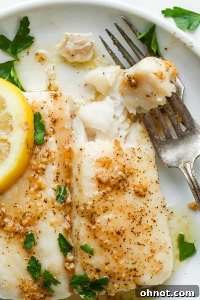 Beautifully plated baked halibut with a generous amount of garlic butter sauce, adorned with fresh lemon and parsley.