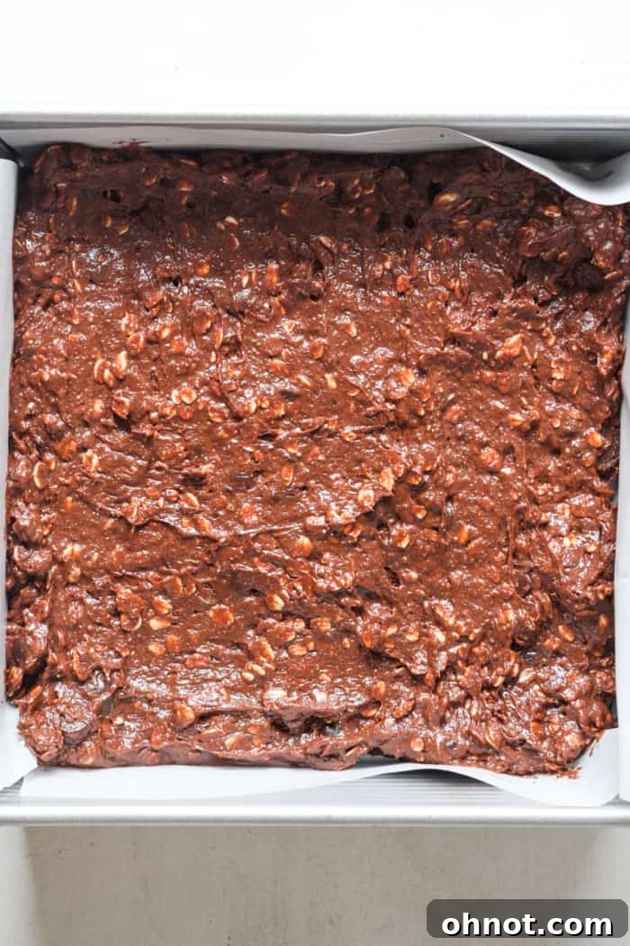Raw lactation brownie batter spread smoothly into a parchment-lined baking pan, ready for the oven.