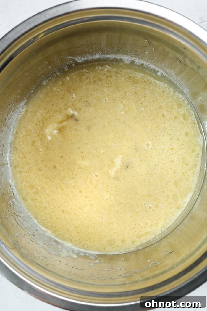 Runny thin bread batter. A mixing bowl containing a light brown, liquid batter, illustrating the initial stage of combining wet ingredients.
