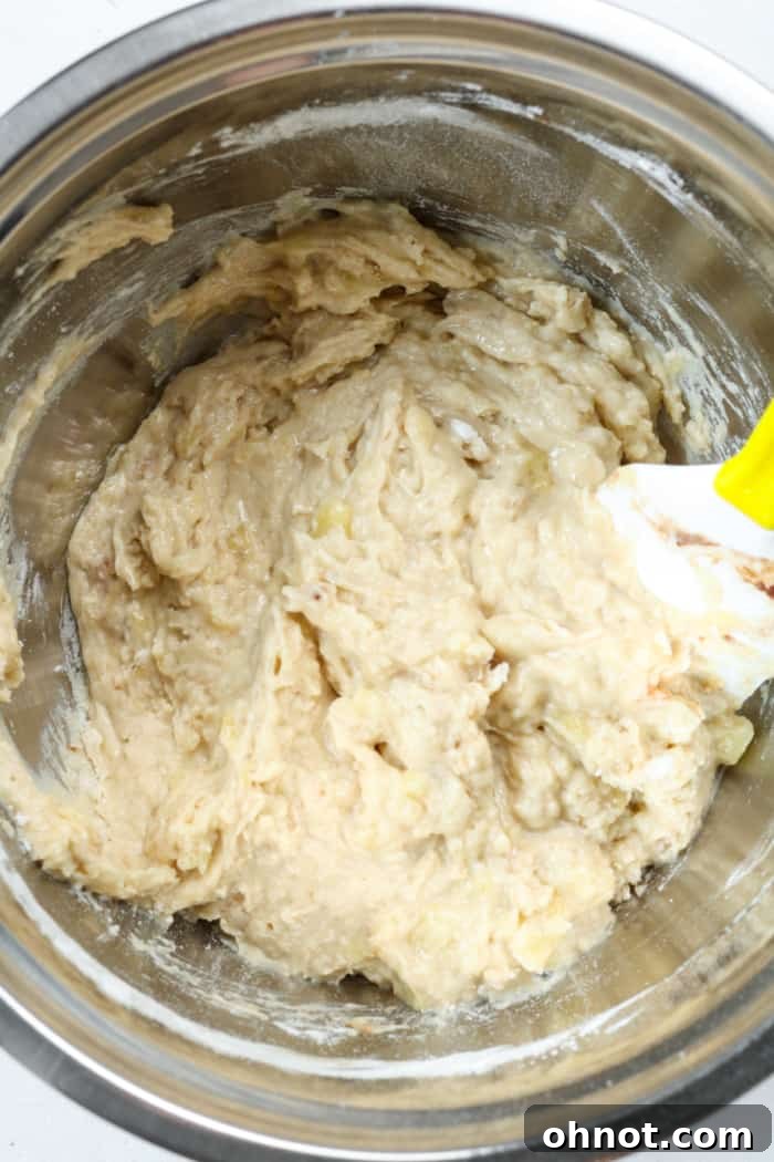 Thick bread dough. A mixing bowl showing a thicker, light brown batter after dry ingredients have been added, ready for the next step.