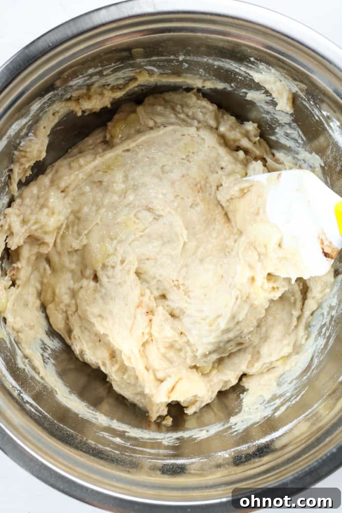 Thick banana bread dough. A close-up of a thick banana bread batter in a bowl, with visible slices of banana gently folded in.