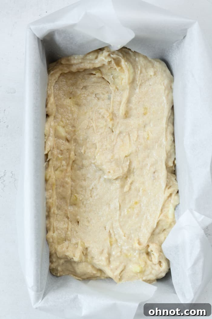 Bread batter in pan. A loaf pan lined with parchment paper, filled with the thick banana bread batter, ready for baking.