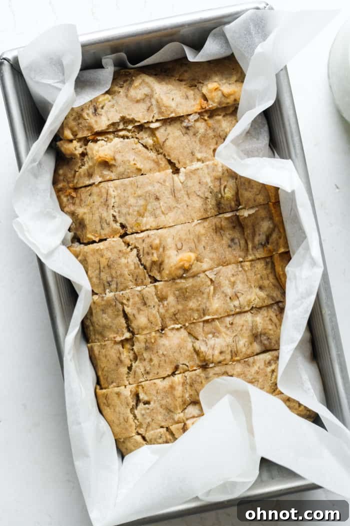 Sliced bread in pan. A perfectly baked loaf of sugar-free banana bread, partially sliced to reveal its moist interior, still in the loaf pan.